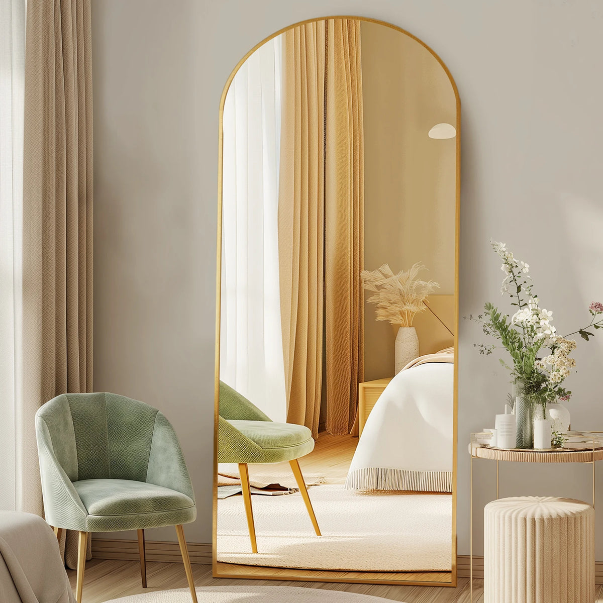 A modern arched full-length mirror with a gold frame reflects soft curtains and a bedroom setting.