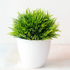 Un vibrant bonzai artificiel vert dans un pot blanc repose sur une surface claire.