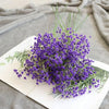A bouquet of purple artificial gypsophila flowers displayed on a white card against a gray fabric background.