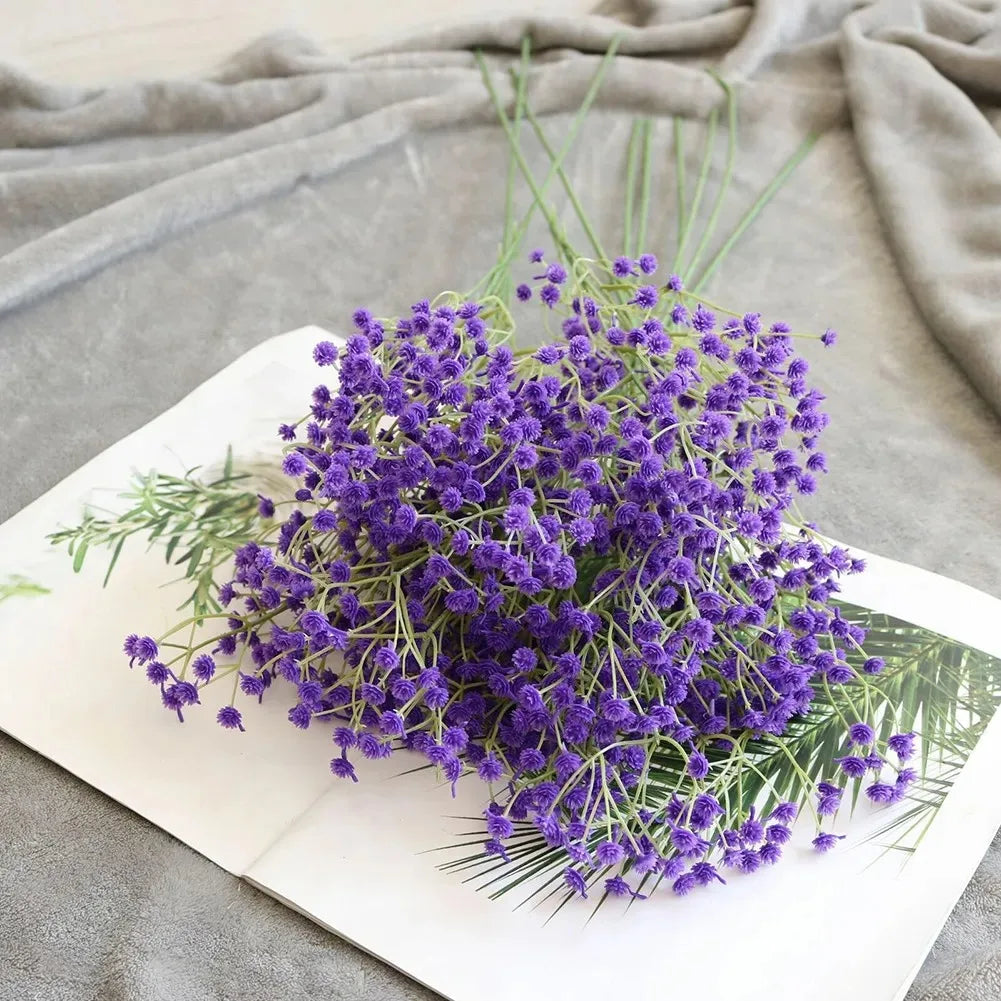 A bouquet of purple artificial gypsophila flowers displayed on a white card against a gray fabric background.