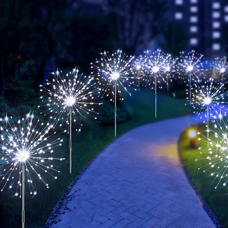 Une rangée de feux d'artifice LED blancs et bleus illuminent un chemin dans un jardin.