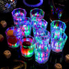 A collection of glowing LED light-up shot glasses arranged on a dark surface.