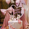 A pink satin bow with long tulle drape is displayed as event decor, featuring a heart shape and elegant fabric folds.
