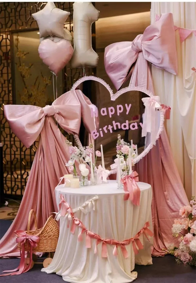 A pink satin bow with long tulle drape is displayed as event decor, featuring a heart shape and elegant fabric folds.