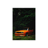 An orange muscle car is parked in a dark, leafy forest setting.