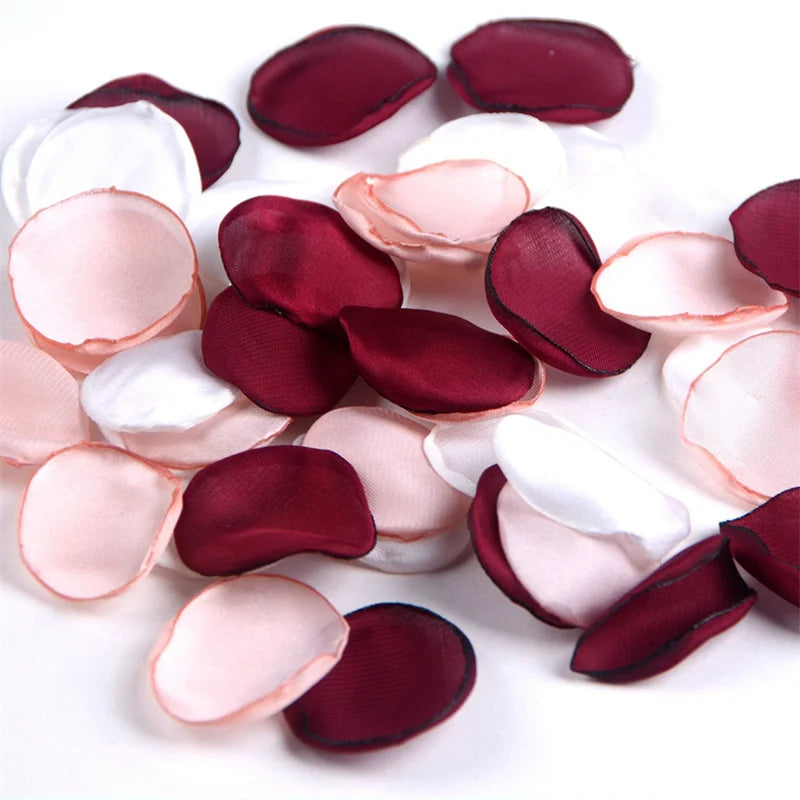 A collection of deep red and pale pink silk rose petals scattered on a white surface.