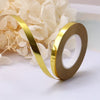 A roll of gold satin balloon ribbon on a white surface next to a cluster of white flowers.