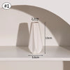 A white minimalist ceramic vase is displayed on a shelf with a shadow cast on the wall.