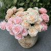 A bouquet of nine silk roses in shades of pink and cream arranged in a rustic vase.