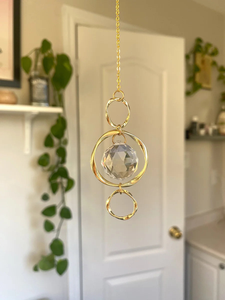 Suspendeur de soleil en cristal ton or avec une sphère facettée transparente suspendue par une chaîne délicate.