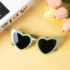 Pair of light green heart-shaped sunglasses resting on a yellow surface next to pink tulips.