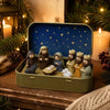 A gold-colored metal box containing a miniature nativity scene with figures and a blue starry background.