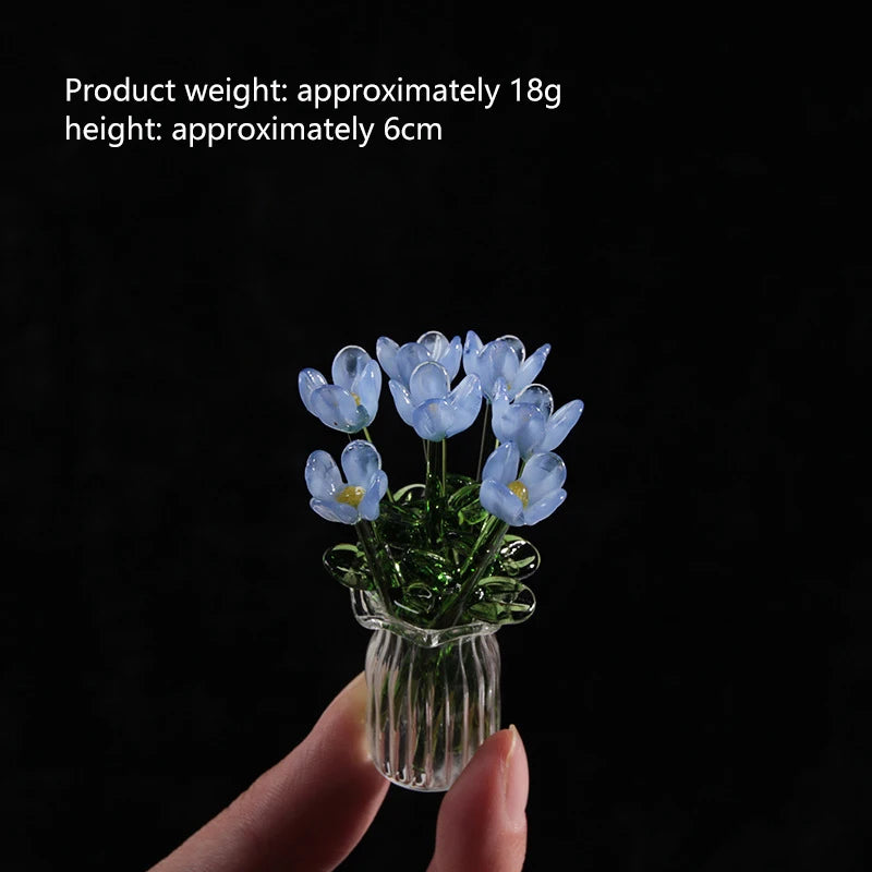 A hand holds a small glass vase filled with light blue handmade glass flowers.