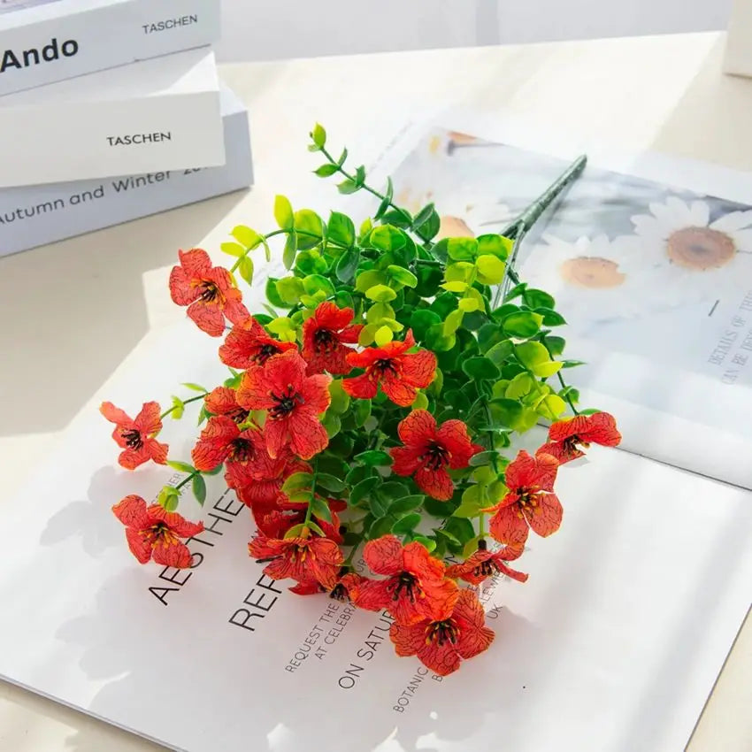 A bouquet of artificial flowers featuring vibrant orange-red eucalyptus leaves and small violet blossoms.