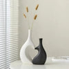 A modern heart-shaped ceramic vase in white and black sits on a white surface next to a window.