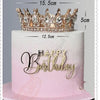 A pink buttercream cake decorated with a crystal rhinestone crown topper and gold lettering that reads Happy Birthday