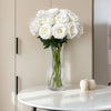 A bouquet of white artificial roses in a clear glass vase displayed on a white table.