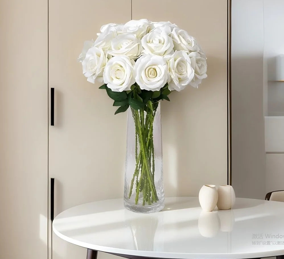 A bouquet of white artificial roses in a clear glass vase displayed on a white table.