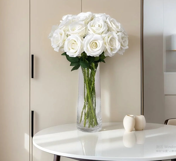 A bouquet of white artificial roses in a clear glass vase displayed on a white table.