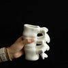 A hand holds a white ceramic vase shaped like vertebrae against a dark background.