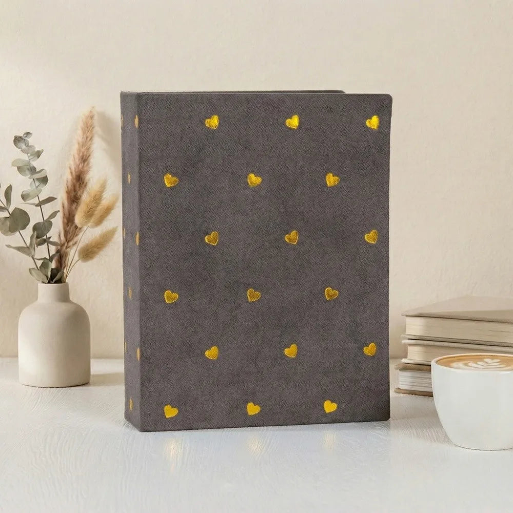 A gray laminated photo album with a pattern of small gold hearts resting on a white surface.