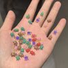 Una mano muestra 50 adornos de uñas de tortugas mini y coloridos esparcidos por los dedos.