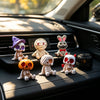 A collection of Halloween resin skeleton mummy figurine toys displayed on a car dashboard.
