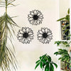 A set of three black metal sunflower wall decor cutouts displayed on a white wall next to a large green plant.