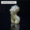 Figura de piedra de labradorita con forma de figura desnuda, reflejando luz sobre una superficie oscura.
