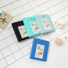 A collection of teal and blue photo albums with instant film inserts displayed on a white grid surface.