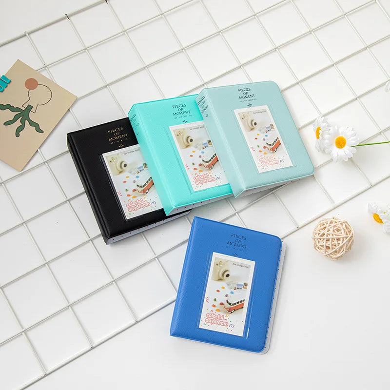 A collection of teal and blue photo albums with instant film inserts displayed on a white grid surface.