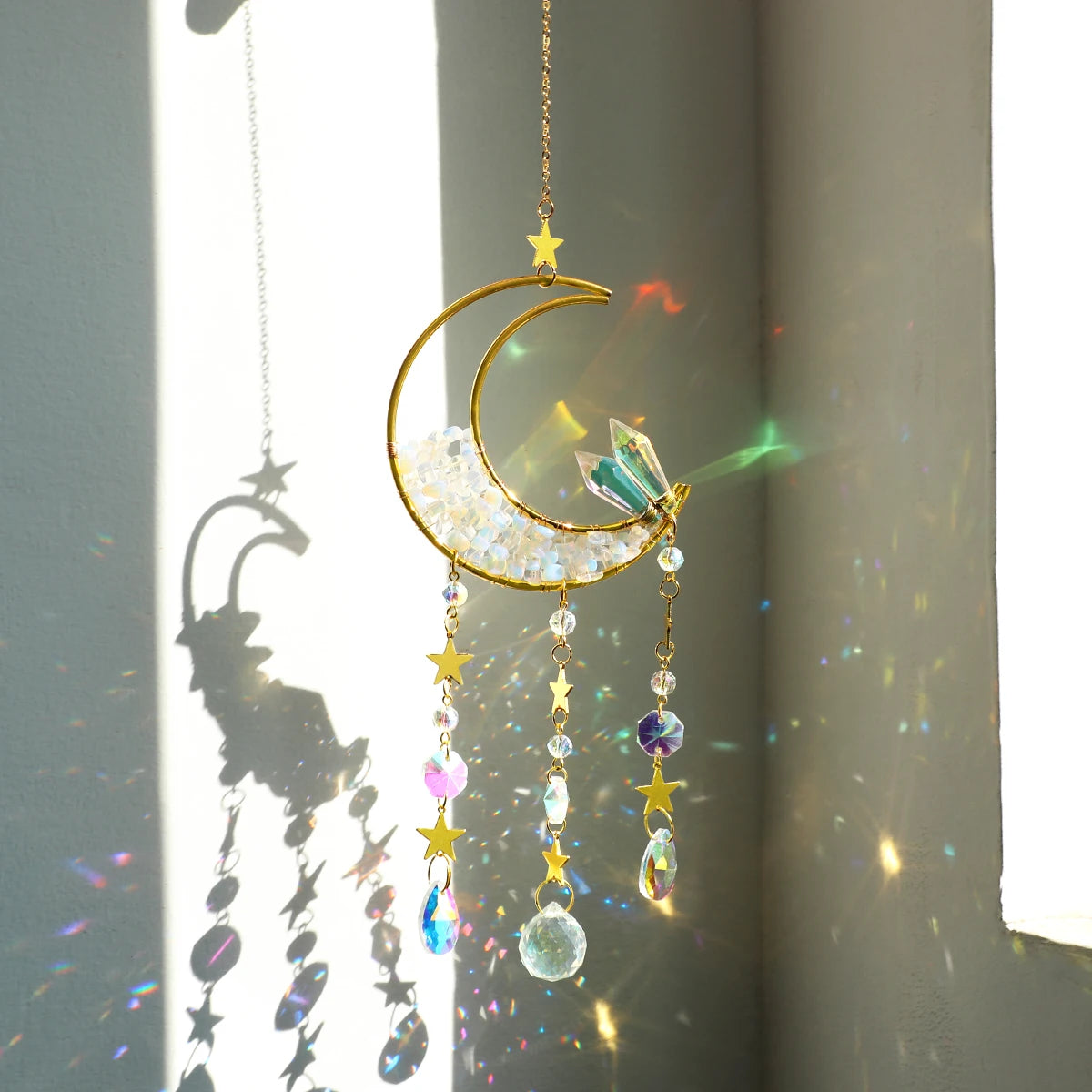 A golden crescent moon dreamcatcher hangs, featuring iridescent crystals and colorful beads, casting light onto a wall.