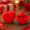 A red 3D printed heart surprise box and a red finger toy are displayed on a wooden surface with scattered red rose petals.
