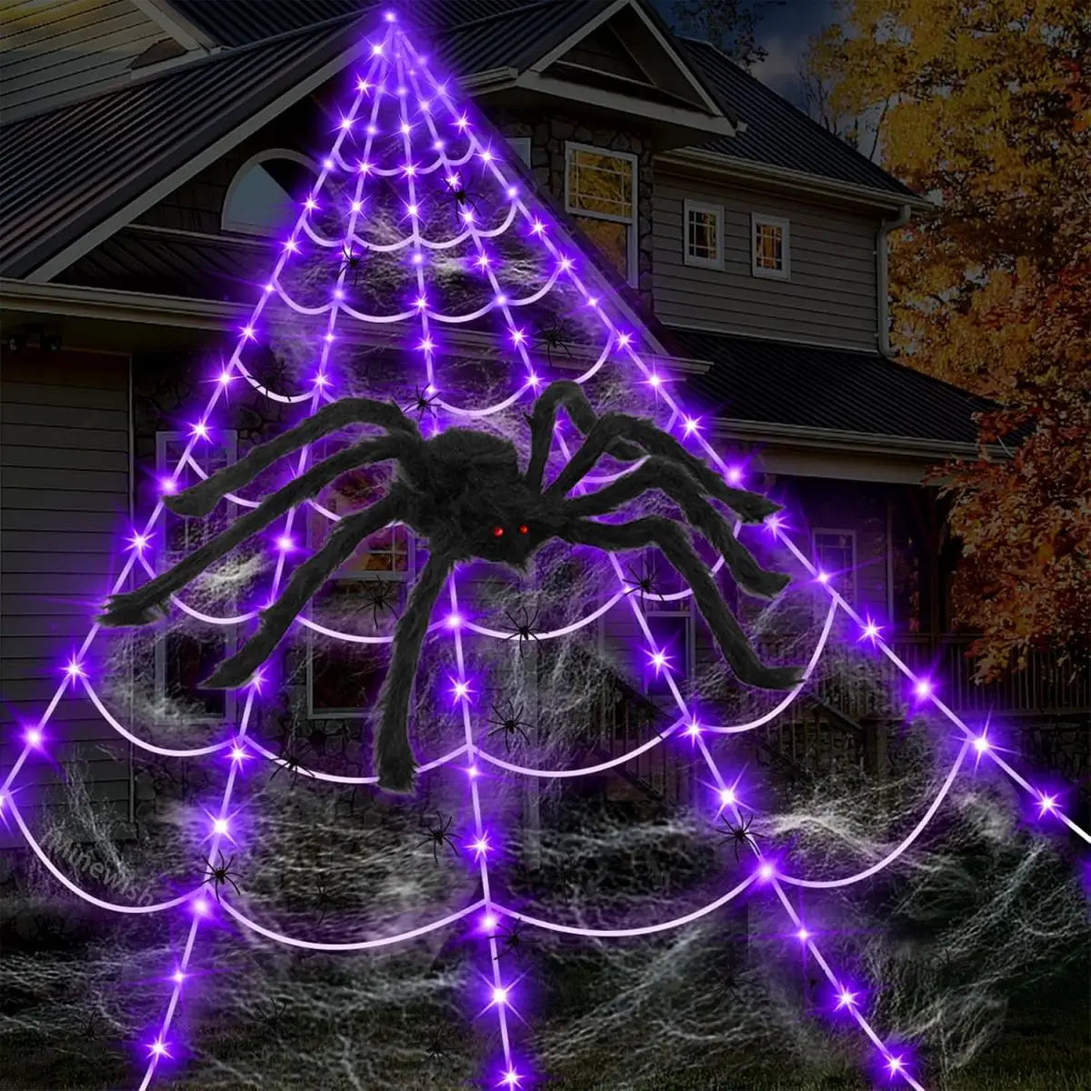 A giant purple spider web illuminated by lights, featuring a large black spider against a house backdrop.