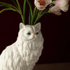 A white ceramic cat figurine with pink tulips emerging from its body.