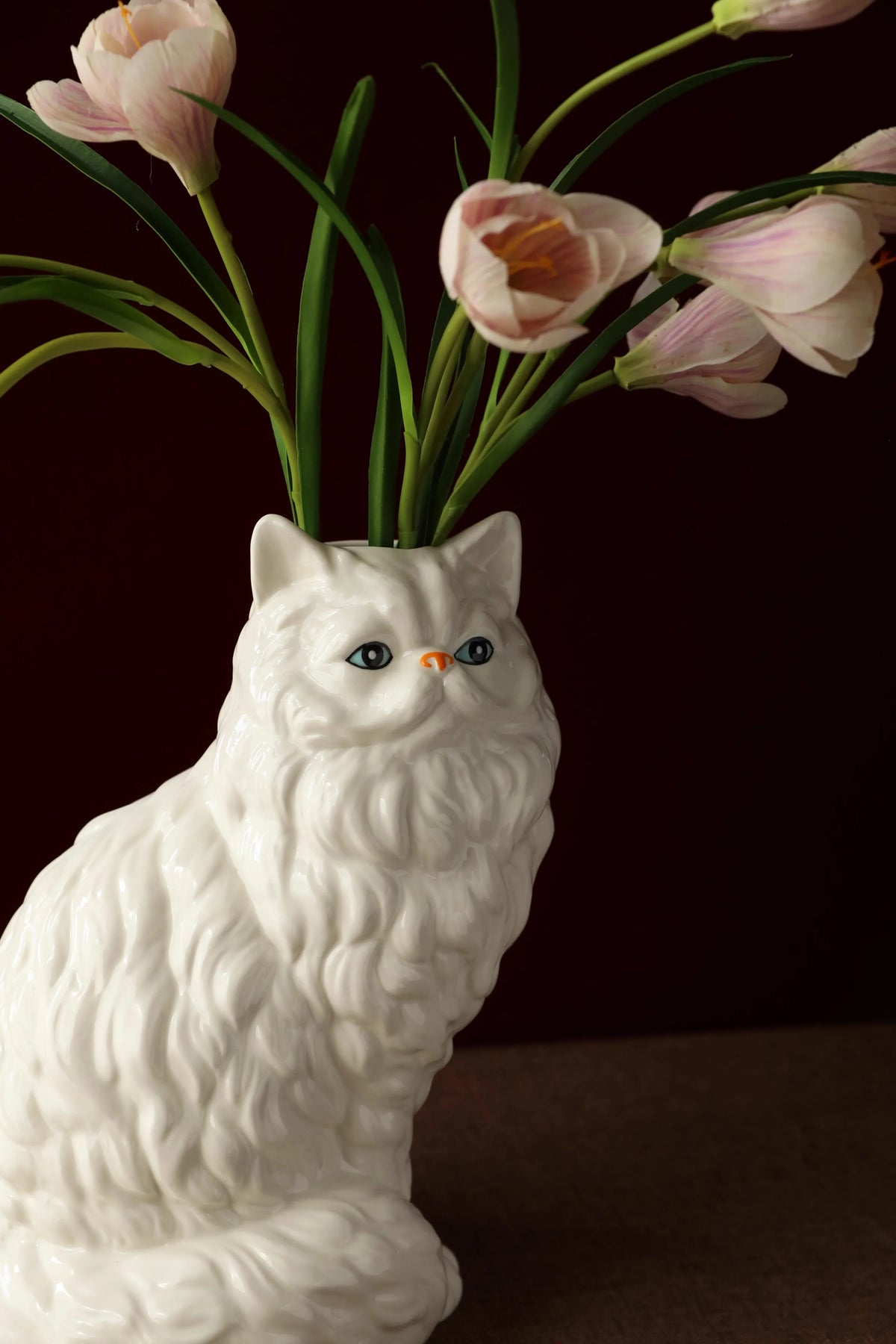 A white ceramic cat figurine with pink tulips emerging from its body.