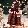 A red velvet Christmas gift box with a green plaid ribbon bow sits on a wooden sleigh in a snowy outdoor setting.