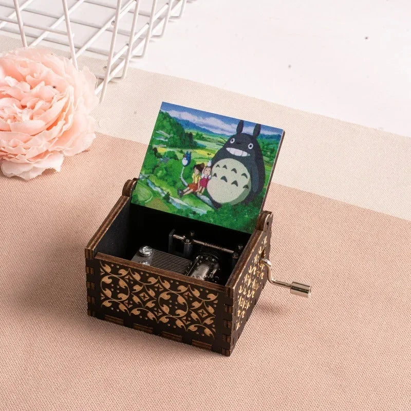A hand-cranked wooden music box featuring a Totoro design, set against a light beige background.