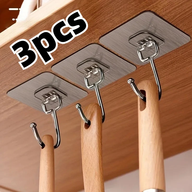 Three silver adhesive wall hooks are shown mounted on a wooden surface for home organization.