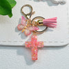 A gold-toned keychain featuring a pink glitter butterfly charm and a pink resin cross charm.