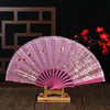 A delicate pink folding fan with plum blossom patterns displayed on a wooden stand.