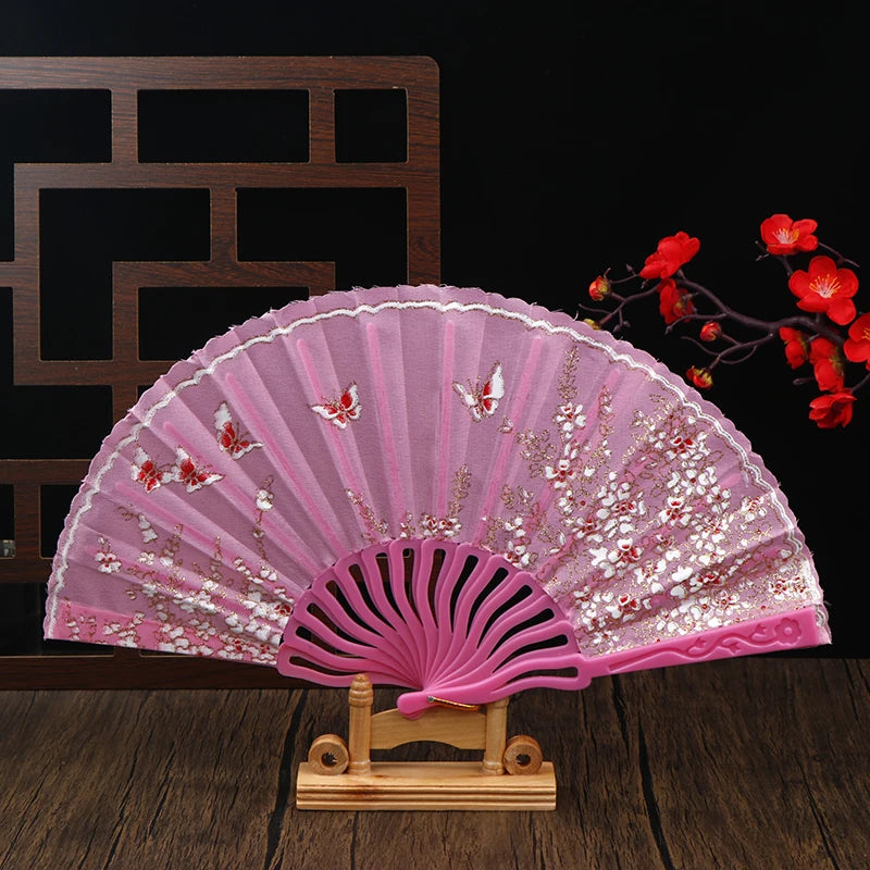 A delicate pink folding fan with plum blossom patterns displayed on a wooden stand.