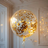 A large, clear balloon filled with gold confetti floats in a well-lit room.
