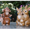 A hand-painted resin garden statue featuring a mother rabbit and her baby, sitting on a stone surface.