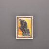A framed painting featuring a dark, expressive figure against a warm orange background.