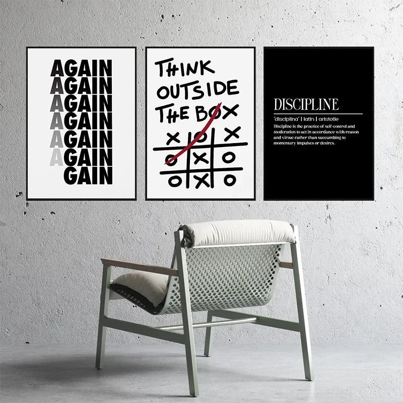 Three black and white motivational quote prints on a gray wall above a light wooden chair.