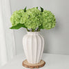 A vase filled with light green artificial hydrangea flowers sits on a wooden coaster.