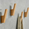 Set natürliche Holz-Wandhaken zum Aufhängen von Mänteln, Taschen und Handtüchern an einer grauen Wand.