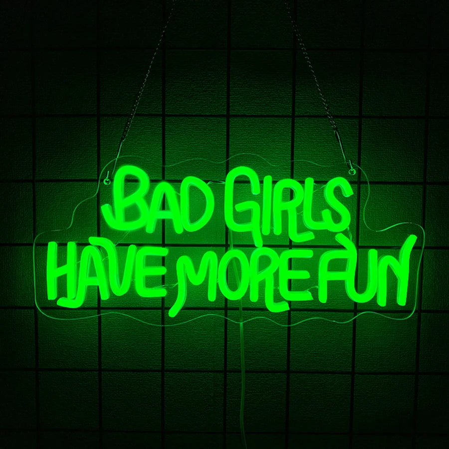 A neon green sign hangs against a dark grid background with the text BAD GIRLS HAVE MORE FUN.