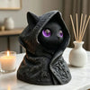 A dark gray gothic hooded cat statue with glowing purple eyes sitting on a white marble surface.